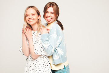 Two young beautiful blond smiling hipster women in trendy summer hipster jeans clothes. Sexy carefree female posing near wall. Trendy and positive models having fun