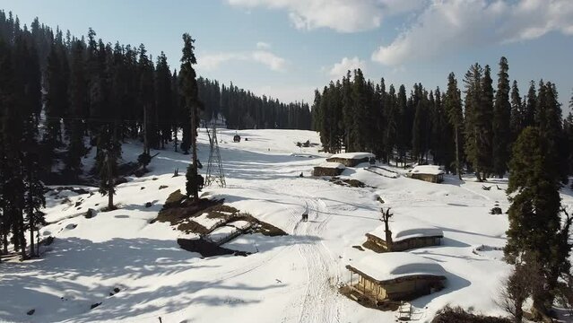 Aerial slow movement around snow covered forest surrounded by pine trees and buildings in Gulmarg