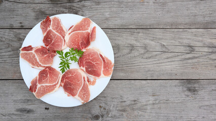 Raw Pork Slice in White Round Plate on old Wooden Table. Slide raw meat on the table decorated with parsley on a white plate