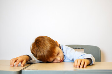the boy is lying on the desk. the student of small classes is tired