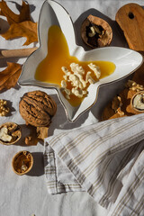 Butterfly shaped plate full of honey and shelled walnuts on white background with wooden cutting board, dry oak leaves.