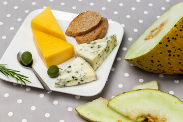 Melon, different types of cheese and olives on plate.