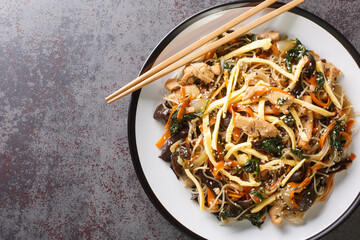 Korean Japchae Stir-fried glass noodles and vegetables closeup on the plate on the table. Horizontal top view from above