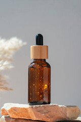 Amber dropper bottle with serum or gel on stone podium. Grey background. Beauty concept for face and body care. Skincare products, natural cosmetic.