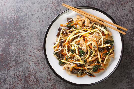 Korean food stir-fried with noodles, meat, mushrooms and vegetables called Japchae closeup on the plate on the table. Horizontal top view from above