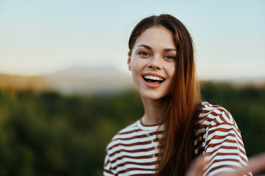 Young woman in a striped t-shirt smiles cutely on a journey against the backdrop of autumn nature