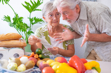 Portrait of worried old senior couple at home table holding grocery receipt discussing for rising...