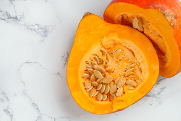 Fresh organic ripe cut pumpkin with seeds. Vegetables on a marble background. Vegetarian and vegan cuisine. Healthy nutrition, diet. Selective focus, top view and copy space