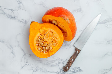 Fresh organic ripe cut pumpkin with seeds. Vegetables on a marble background. Vegetarian and vegan cuisine. Healthy nutrition, diet. Selective focus, top view and copy space