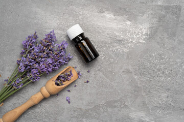 Bottle with aroma essential oil and lavender flowers on gray concrete background. Top view, flat lay. Spa and skin care product.