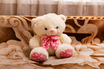 A polar teddy bear with a pink bow on the couch. Retro style