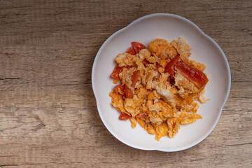 Stir fried egg with tomato,Scrambled eggs with tomatoes and white plate on wooden background
