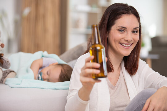 happy woman drinking a beer while baby sleeps