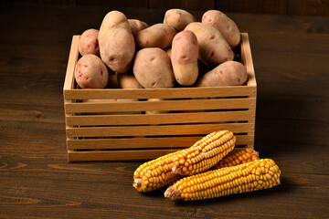 wooden box full of potatoes and corn cobs on dark wooden background