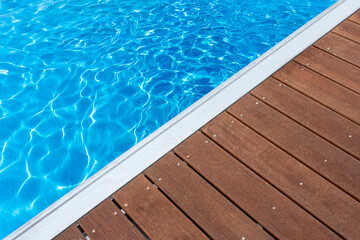 Fototapeta na wymiar Plage bi-matière de piscine bleue , plage bois et margelle en aluminium 
