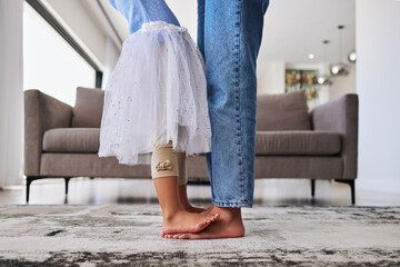 Feet, child and mother teaching a dance ballet movement on the living room floor together in their...