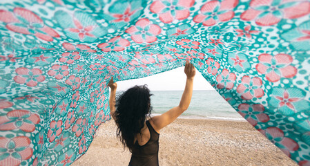 A woman holds a headscarf over her head and the wind blows her shawl