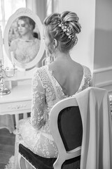 Young beautiful bride with wedding bridal hairstyle with pearls and crystals  near the boudoir table in the bedroom. wedding morning
