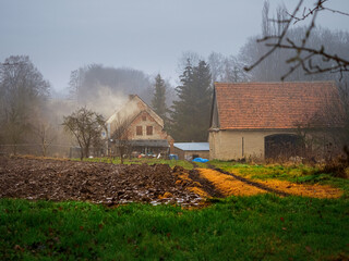 plowed field covered with a snow and old farmhouse on a background in an old village in a rainy...