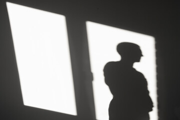 Silhouette of a man on the reflection of sunlight from the window. Abstract background in the dark of an empty room.