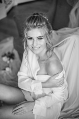 Young beautiful bride with wedding hairdo and makeup in the morning wearing a white silk negligee in the bedroom. wedding morning