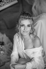 Young beautiful bride with wedding hairdo and makeup in the morning wearing a white silk negligee in the bedroom. wedding morning