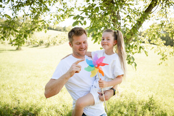 Fototapeta premium Father and daughter cuddle and have fun outside in nature with colorful pinwheel and are happy