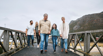Family, walking and travel with a girl and grandparents holding hands on a pier while on holiday or...