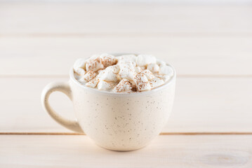 Hot cocoa with marshmallows in a white mug on a wooden table.