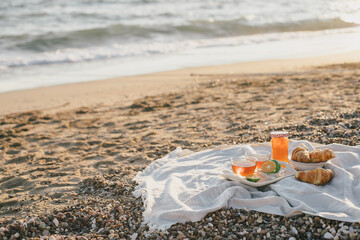 Tasty summer picnic with fresh tea and croissants on the beach at sunset.