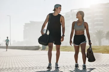  Sports, personal trainer and woman in fitness walking with a soccer ball for cardio exercise, workout and training session. Smile, wellness and happy couple enjoy a healthy city lifestyle in summer © Allistair F/peopleimages.com