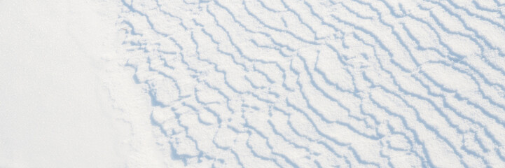Beautiful winter background with snowy ground. Natural snow texture. Wind sculpted patterns on snow surface. Wide panoramic texture for background and design.