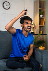 vertical shot of over Excited young man shouting by raising hands while watching live sports match...