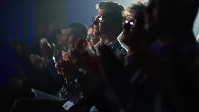 Young Man Sitting in a Crowded Audience at a Business Conference. Male Attendee Cheering and Clapping After a Motivational Keynote Speech. Auditorium with Young Successful Businesspeople.
