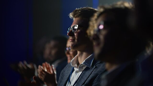 Close Up Portrait of a Handsome Young Businessman in a Dark Crowded Auditorium at a Startup Summit. Young Man Applauding After a Successful Presentation. Entrepreneur Happy with the Event Speaker.
