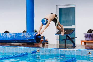 latin teenager man swimmer athlete wearing cap and goggles in a swimming training holding On...