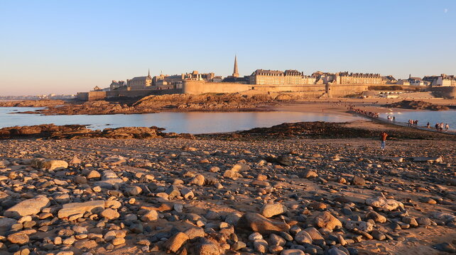Panorama sur les remparts de la vieille ville de Saint-Malo, au bord de la mer, en Bretagne, depuis l&rsquo;&icirc;le du Grand B&eacute;, avec une plage de galets au premier plan, au soleil couchant (France)