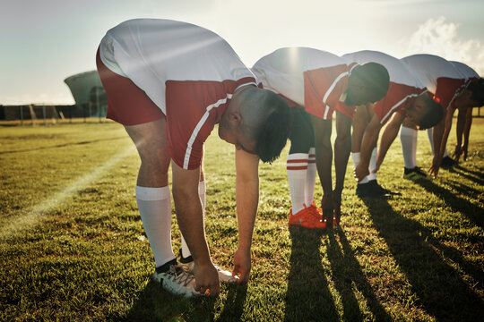 Team, stretching and legs in soccer training, warm up or exercise on field in sunshine at game. Man, football and group together for workout, teamwork and fitness before match, competition or sports