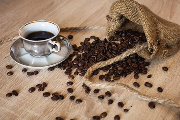 Roasted coffee beans in little bag with ropes and cup of coffee with drink on dark brown wooden...