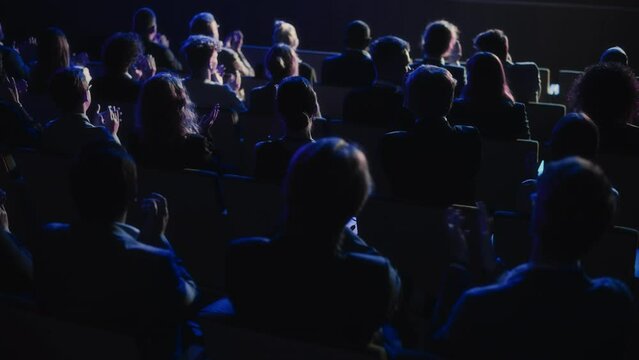 Audience Full of Business People Clapping in Dark Conference Hall During an Inspiring Keynote Presentation. Business Technology Summit Auditorium Room Full of Delegates. Slow Motion Footage.