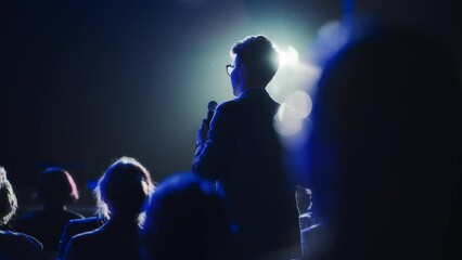 Male Asking a Question to a Speaker During a Q and A Session at an International Tech Conference in a Dark Crowded Auditorium. Young Specialist Expressing an Opinion During a Global Business Summit.