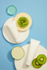 White kiwi puree on a beige tray, next to the white cream tube on the white round platform. On the next platform, a white bottle sample, kiwis slices, and mask.