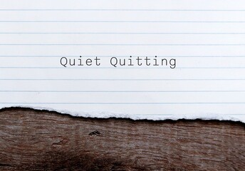 Torn paper on wood background with words QUIET QUITTING, latest workplace buzzword when employees has limited their tasks, avoid working longer hours, get the job done to improve work-life balance