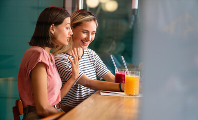 Portrait of two beautiful women having fun, using phone together and chatting in cafe