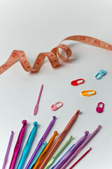 Multicolored crochet hooks of different diameters on a white background with centimeter orange tape...
