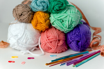 Multicolored crochet hooks of different diameters next to skeins of thread, markers and orange...