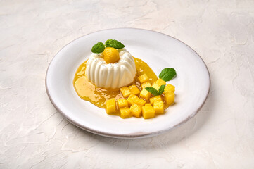 Panna cotta homemade with natural vanilla pod on white plate, mango syrup and mint, high key