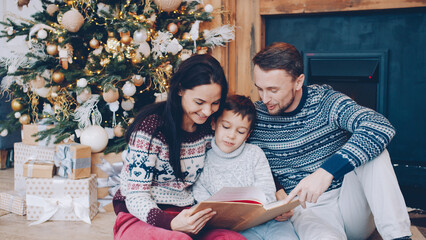Family mother, father and son are reading book and talking on Christmas Eve at home, people are...