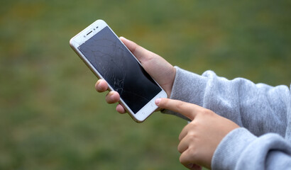 The child is holding a broken smartphone in his hands. Mobile phone breakdown, cracks on the...