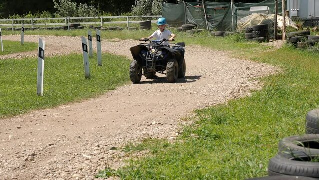 An active little boy rides a large ATV on a dirt road in an adventure park in summer in sunny weather.